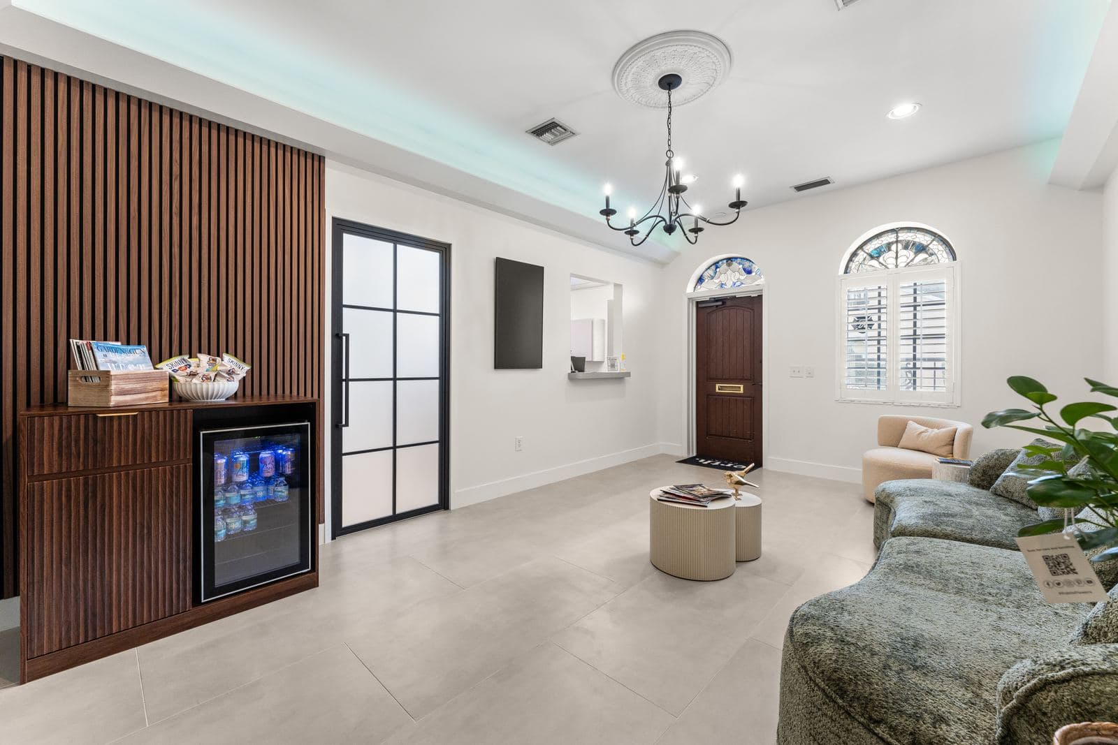 The erth. dental reception area with a chandelier, a walnut refreshment cabinet and an arched window over the front door
