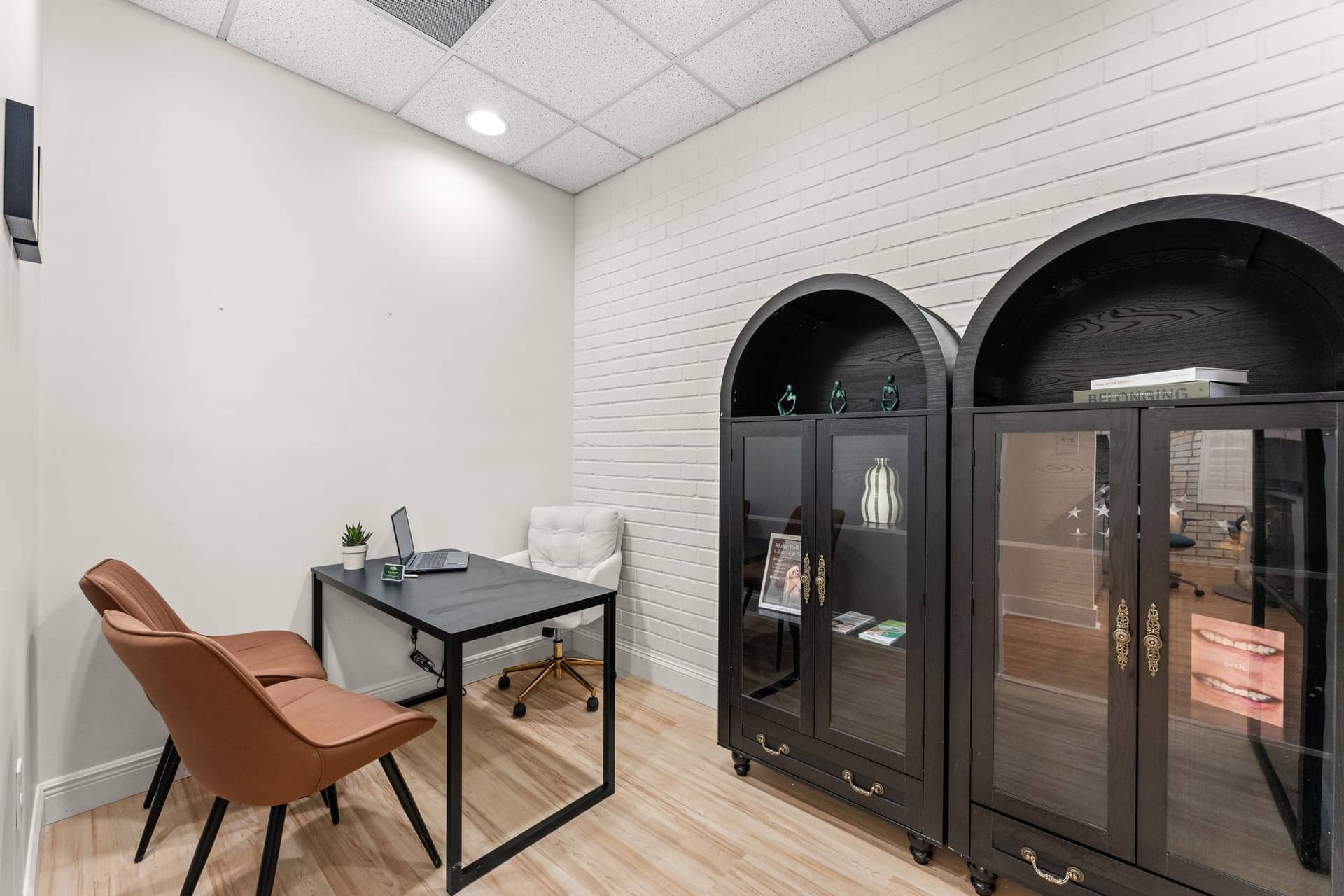 A consultation room at erth. dental with a desk, a laptop and two leather chairs beside black arched display cabinets