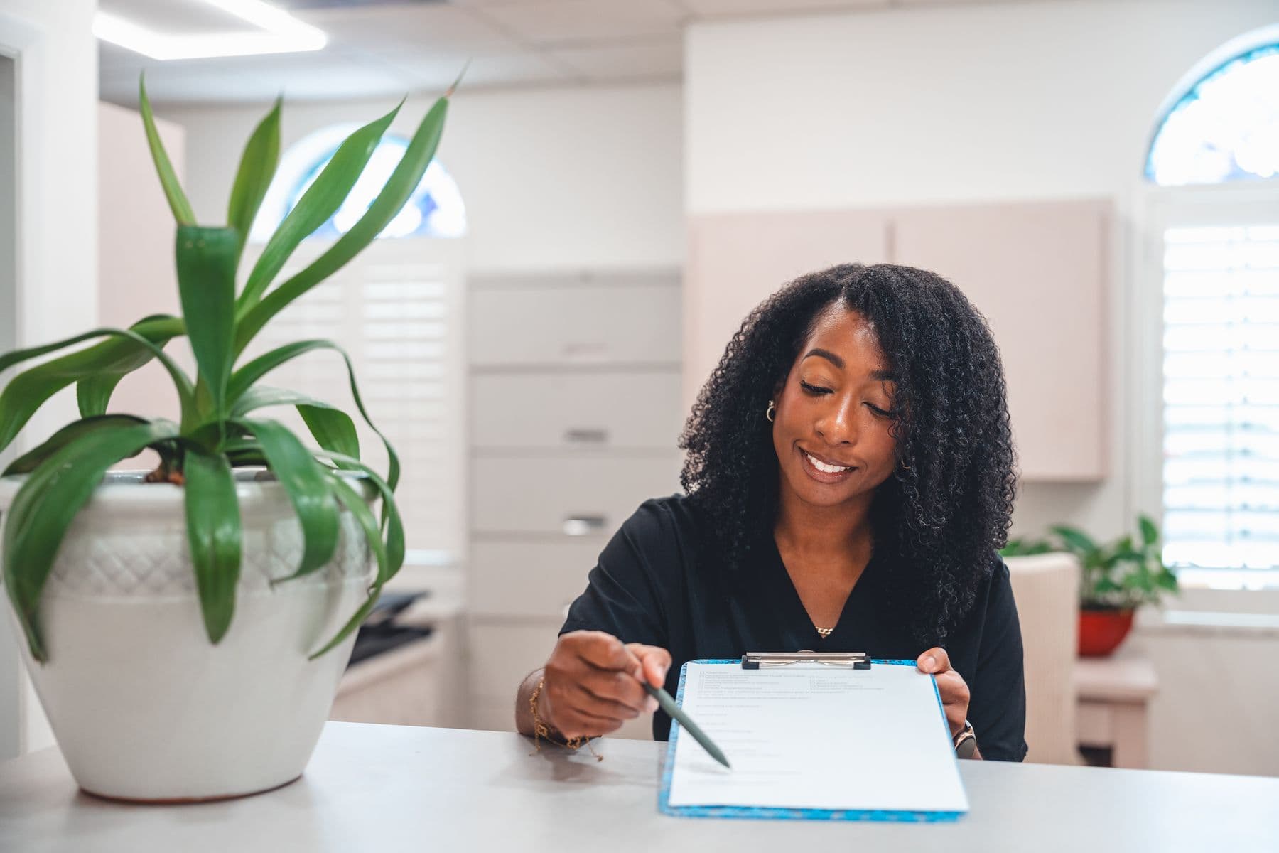 A team member at the front desk smiling as she points to a form on a clipboard