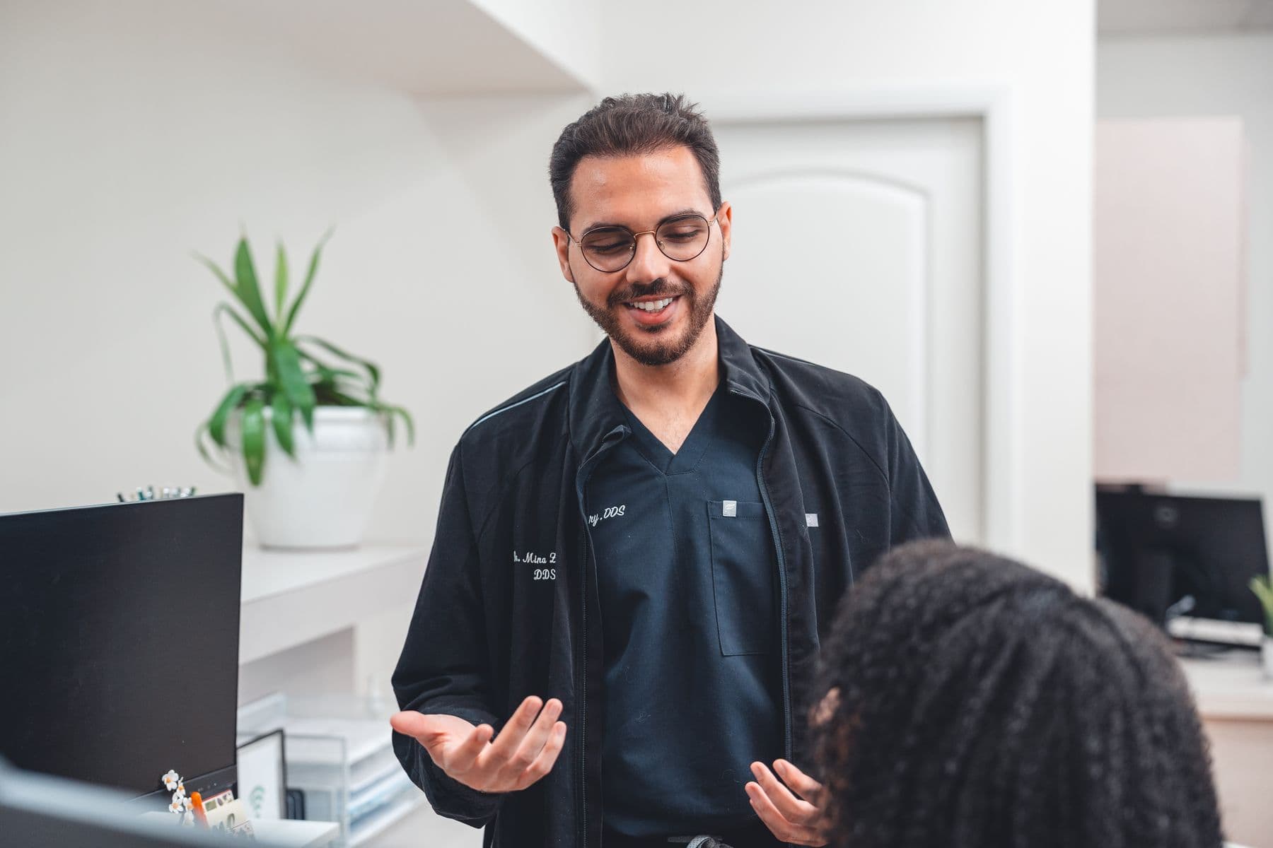 Dr. Mina Zakhary smiling and gesturing as he talks with a patient at the front desk