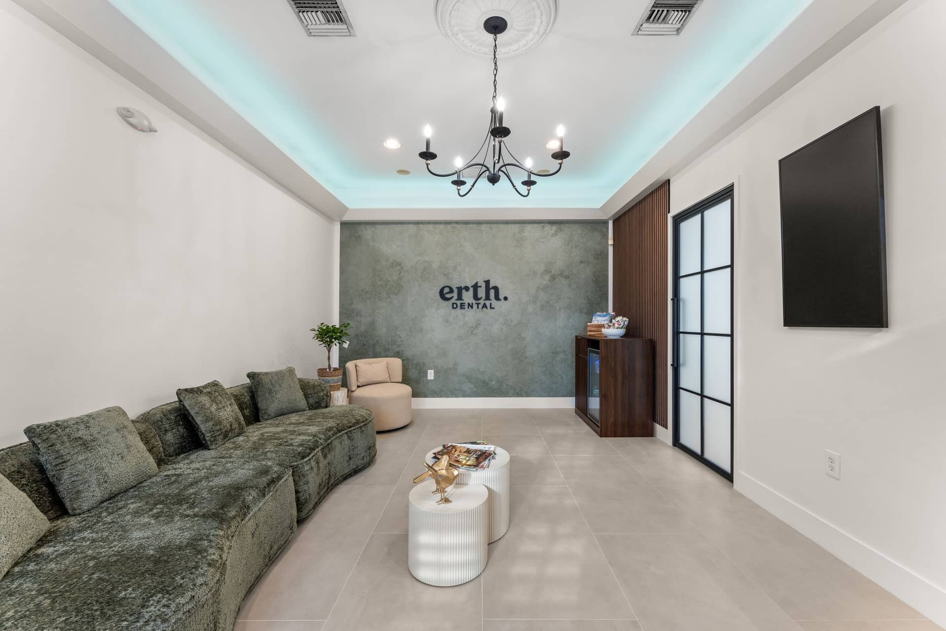 The erth. dental lounge with a green velvet sofa, a chandelier and the practice name on a sage plaster wall
