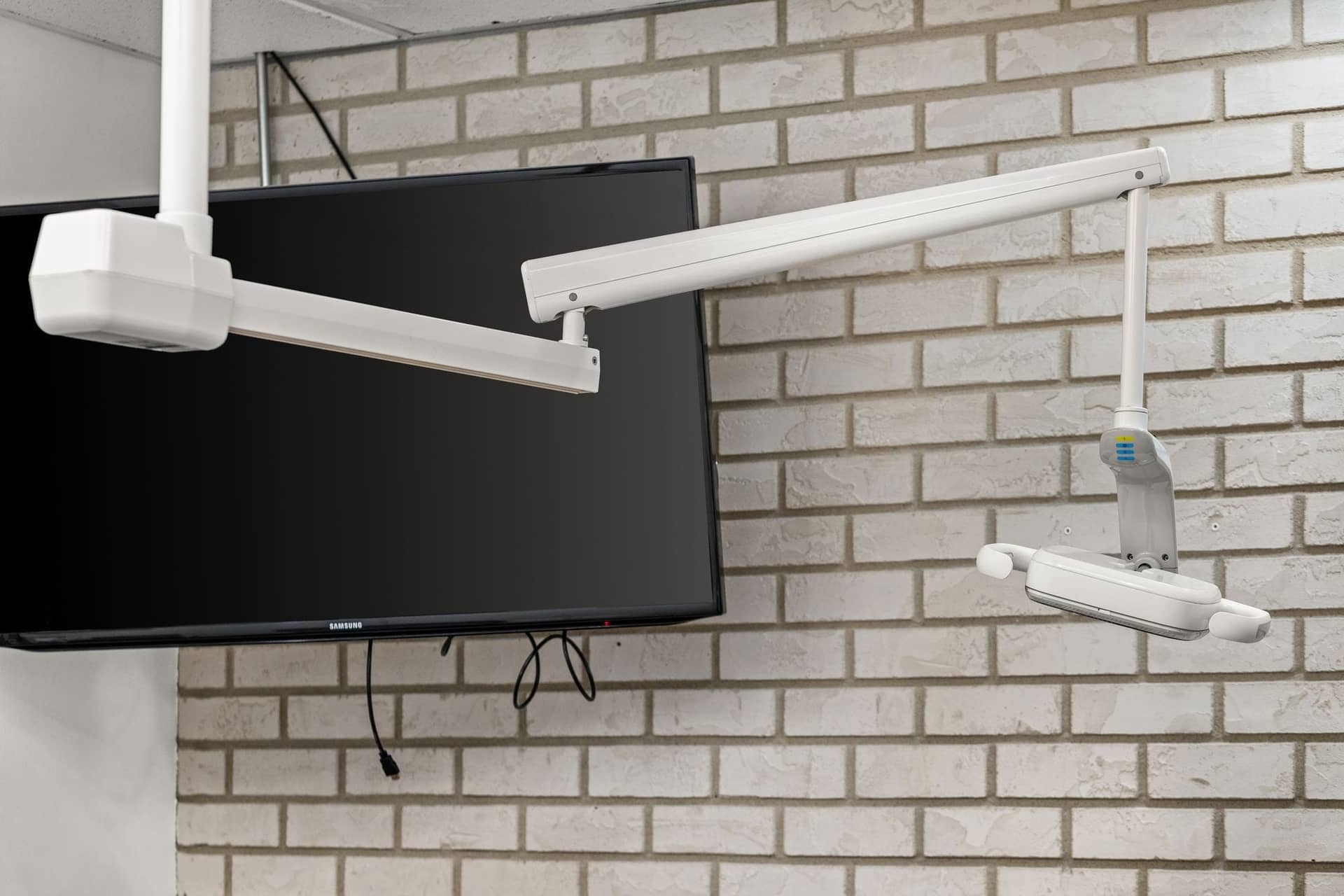 A dental light and monitor mounted on a white brick wall in a treatment room at erth. dental
